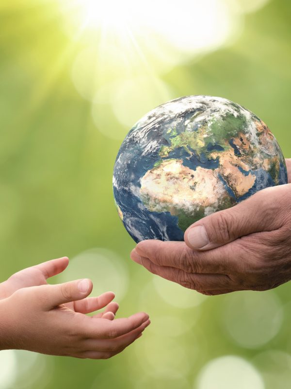 Close up of senior hands giving small planet earth to a child over defocused green background with copy space