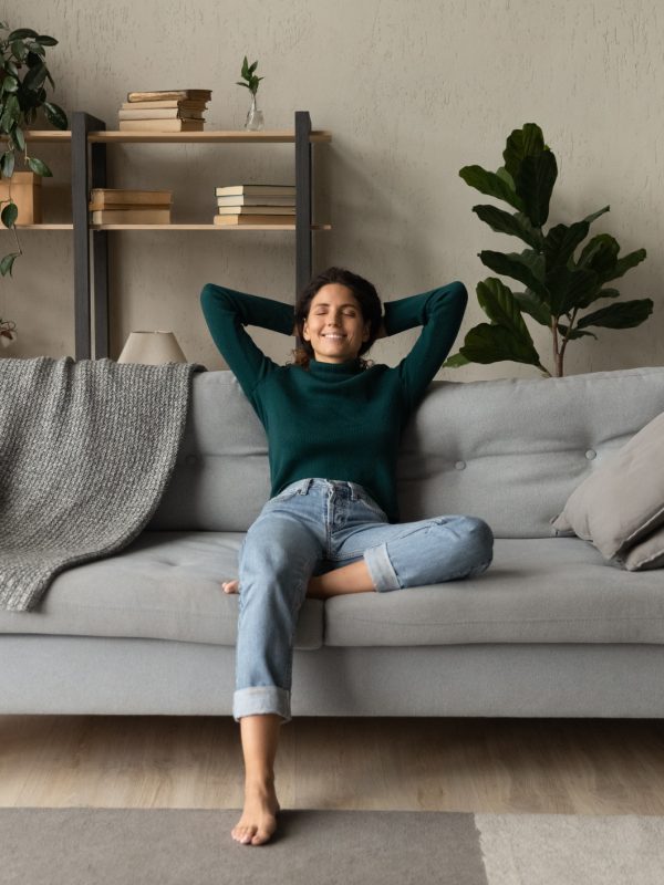 Sweet idleness. Lazy young hispanic lady sit in relaxed pose on big comfy sofa at living room interior breath air dream imagine. Successful female new flat apartment buyer rest at home feel pleasure